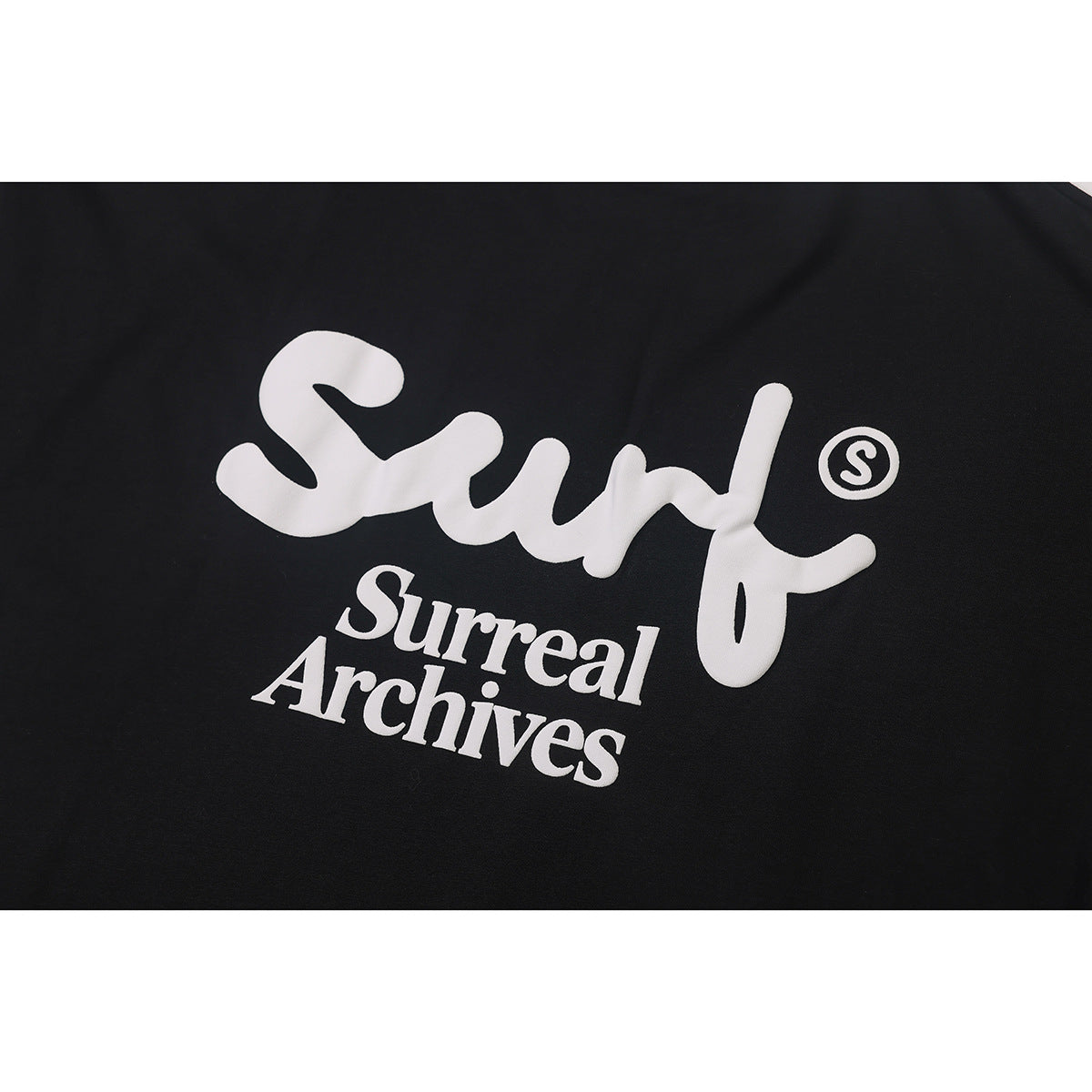 Close-up of a large white “Surf” and “Surreal Archives” graphic printed on black fabric.