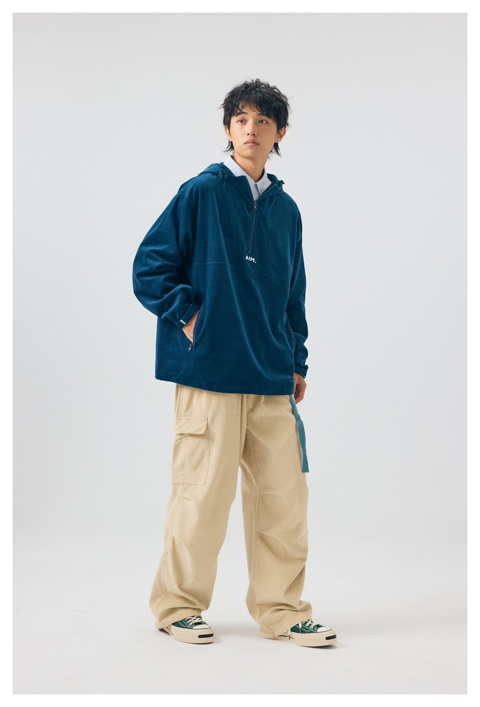 Model wearing blue hooded half-zip jacket with hand in zip pocket, beige cargo pants, three-quarter view