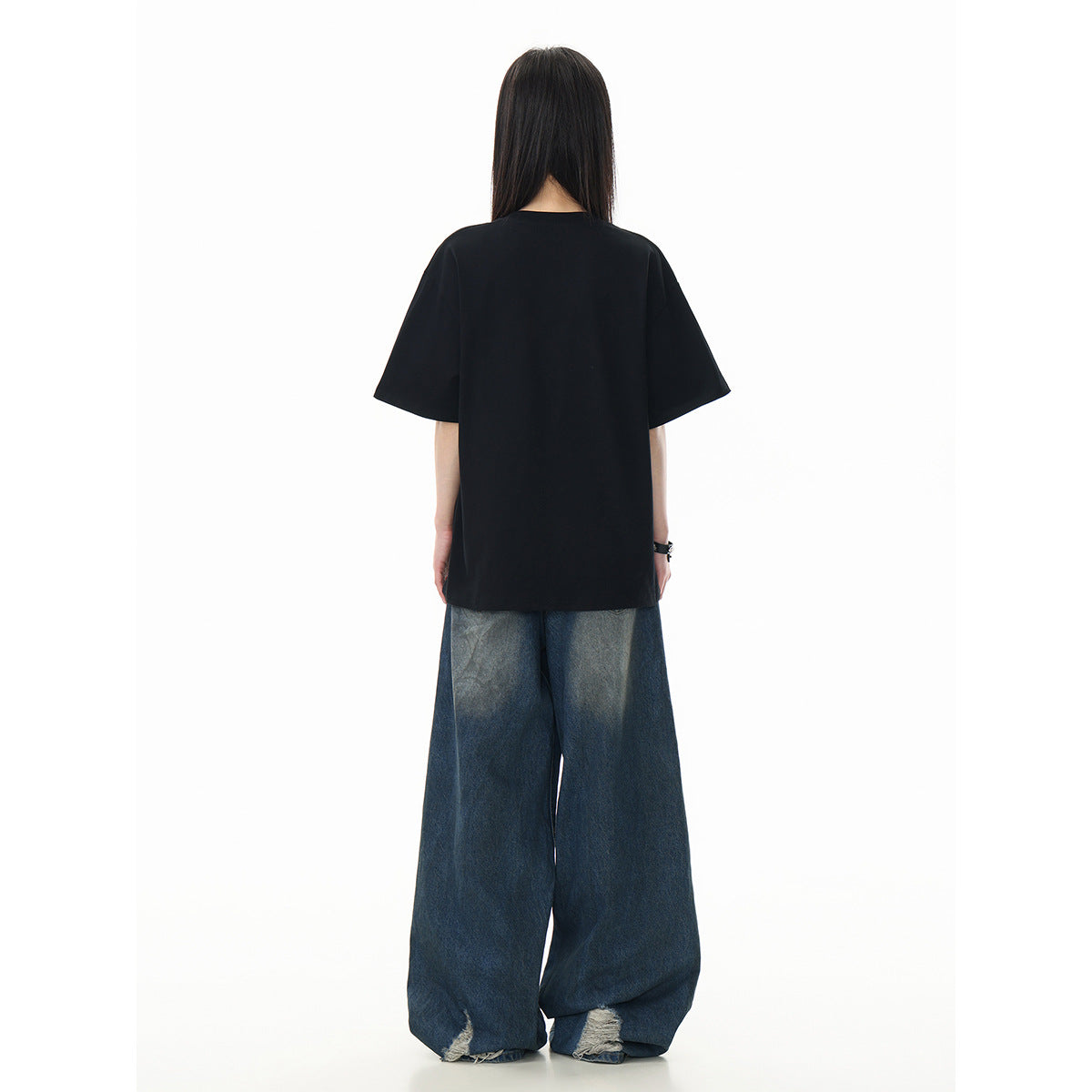 Back view of a model wearing a plain oversized black T-shirt and wide-leg blue jeans.
