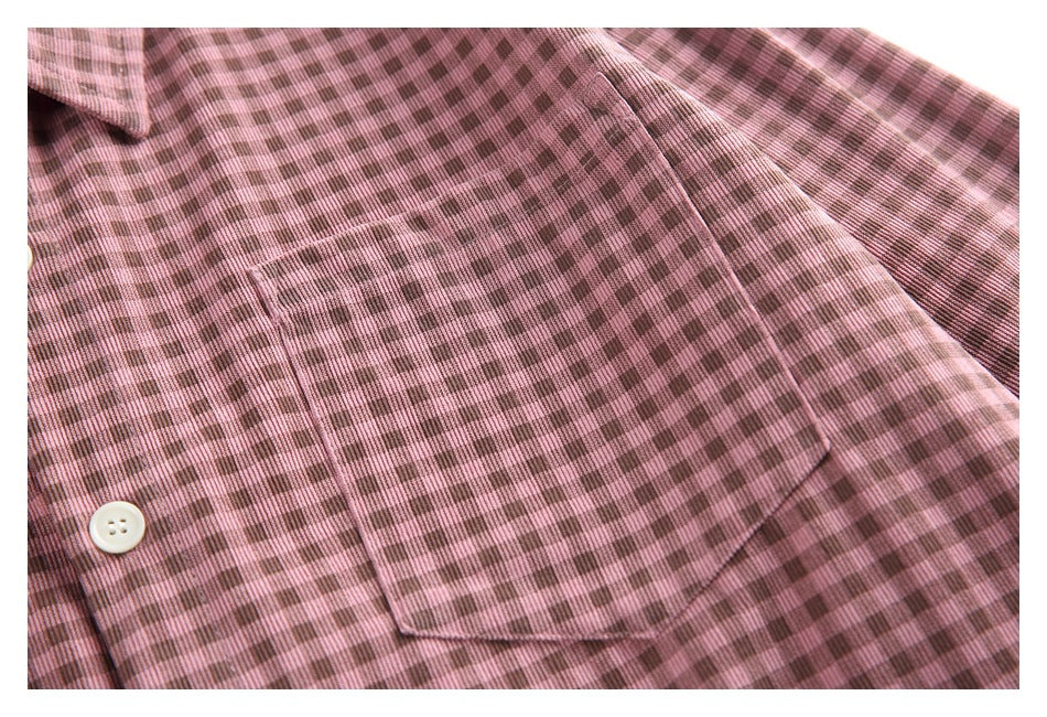 Close-up of the dusty pink and brown check shirt's angled chest pocket and a white button.