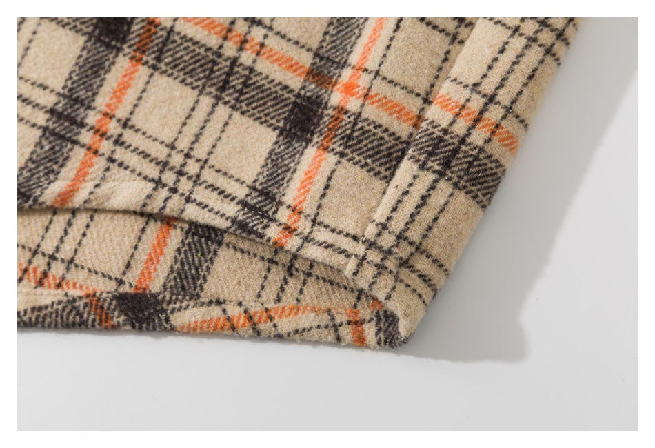 Close-up of the folded hem of a beige shirt with orange and dark plaid lines.