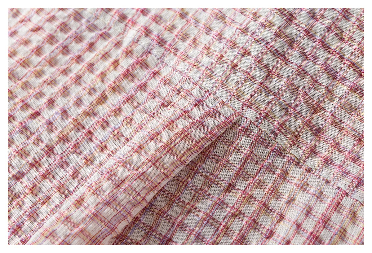Close-up of folded cream plaid fabric with a raised stitched edge and pink, red, and muted yellow lines.