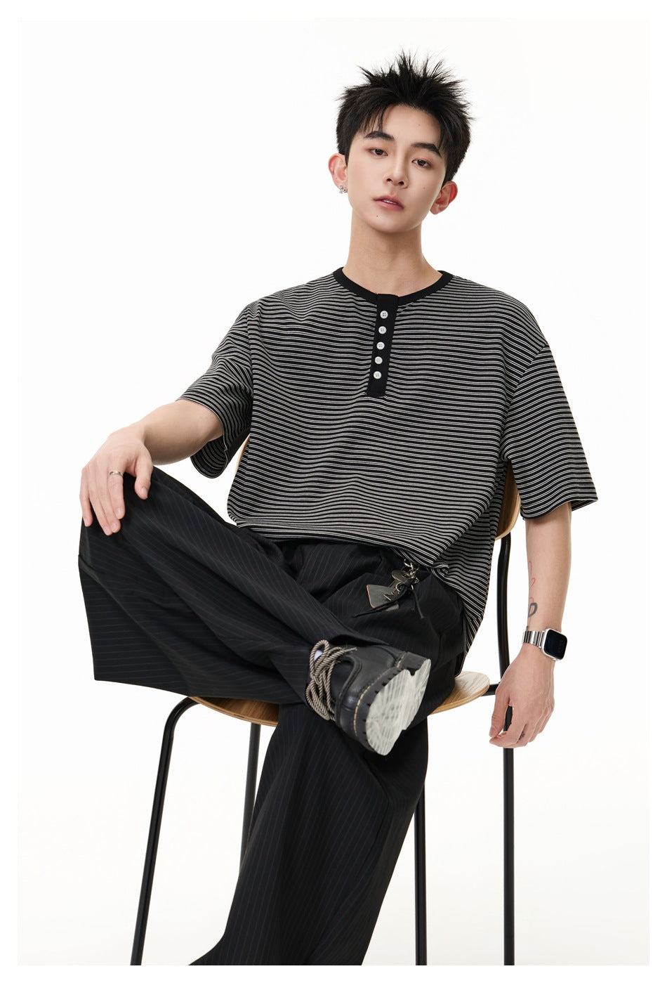 Model seated in a black and gray striped short-sleeve henley with a black button placket.