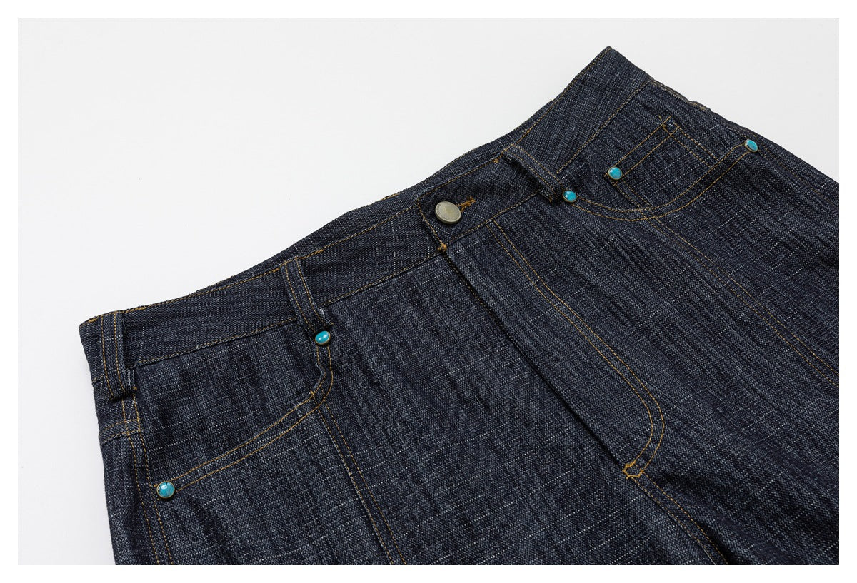 Angled close-up of the pants’ front waistband, fly, pockets, contrast stitching, and turquoise-colored rivets.