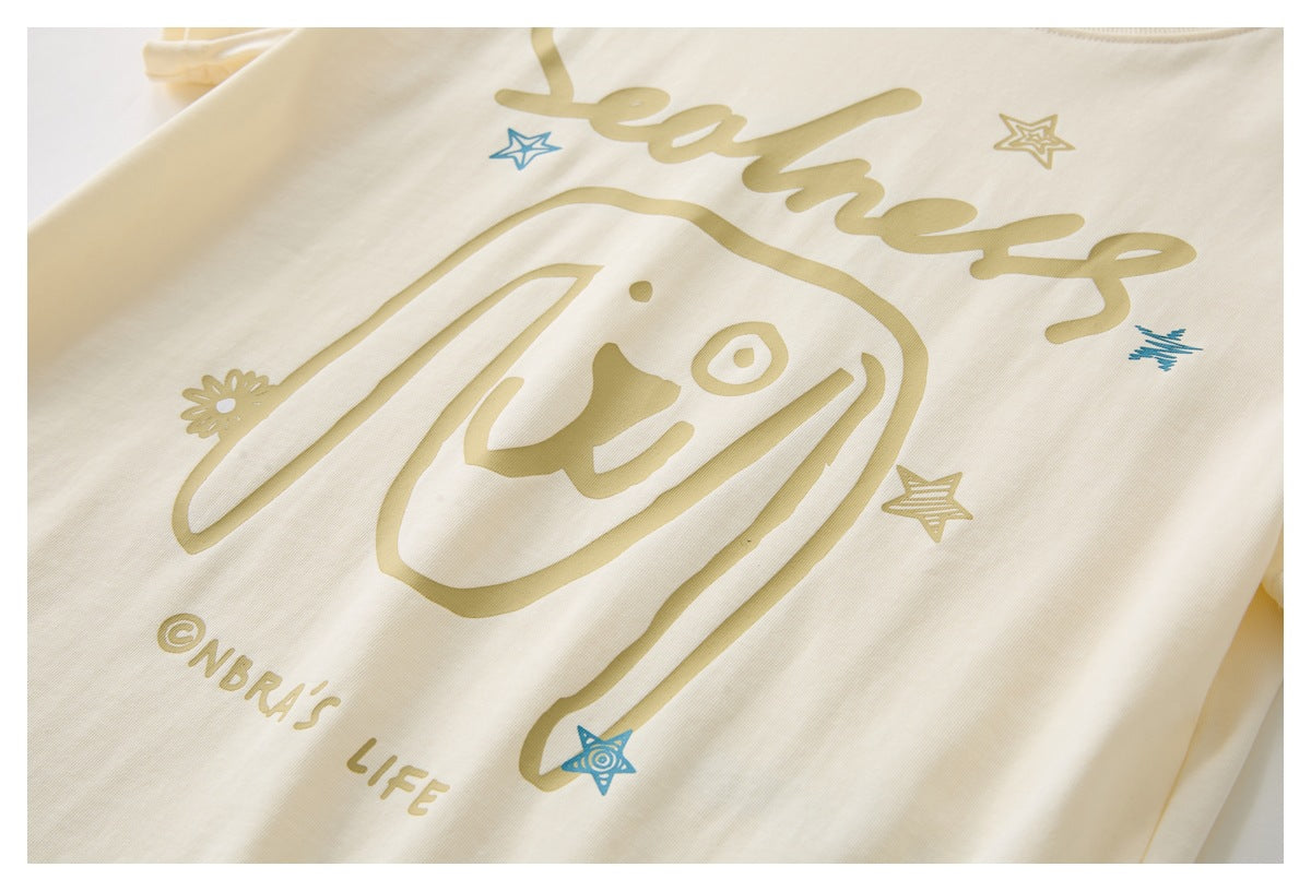 Close-up of a cream garment with a stylized face, stars, and tan and blue printed graphics.