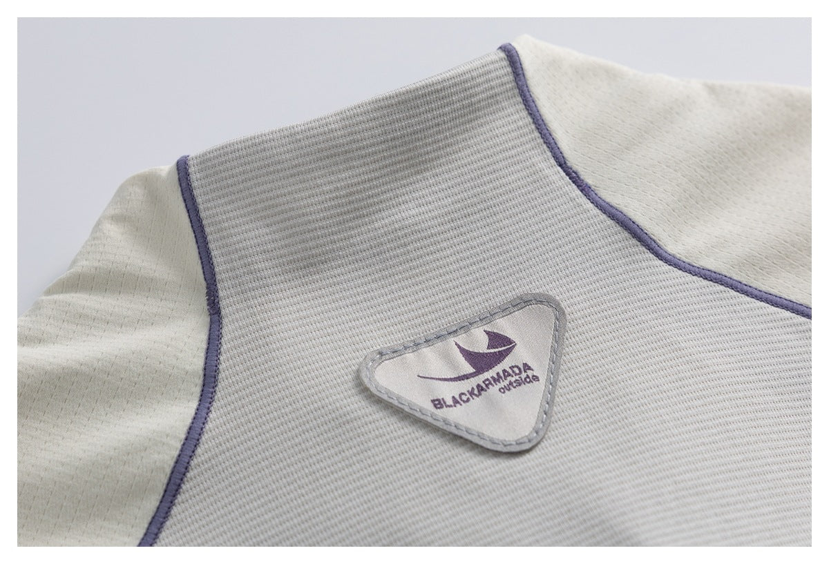 Close-up of a light gray garment with purple piping and a sewn sailboat logo patch.