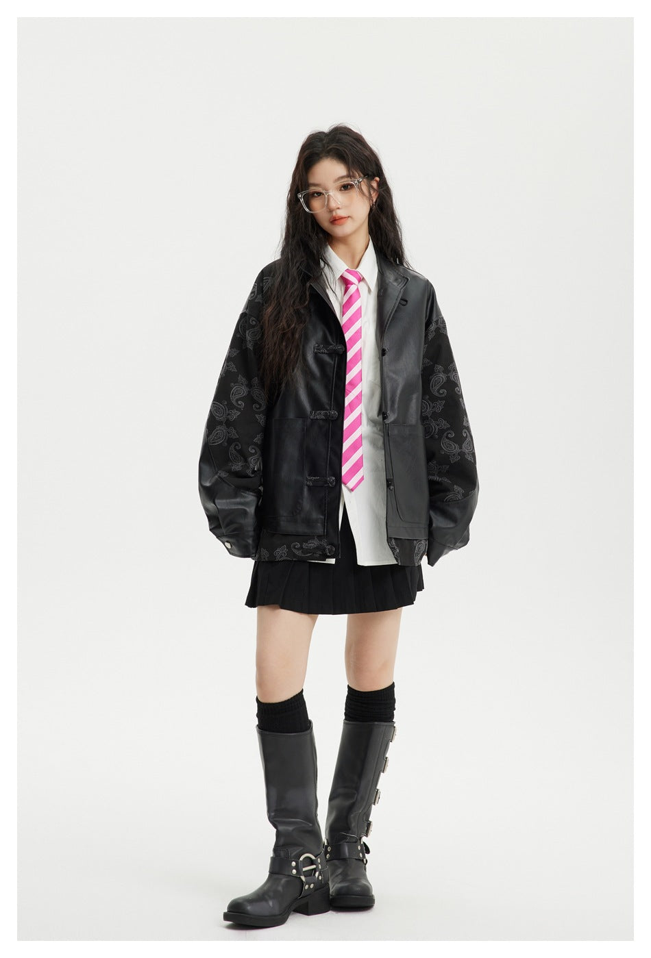 Model wearing an oversized black faux-leather and paisley jacket open over a white shirt, pink striped tie and black skirt