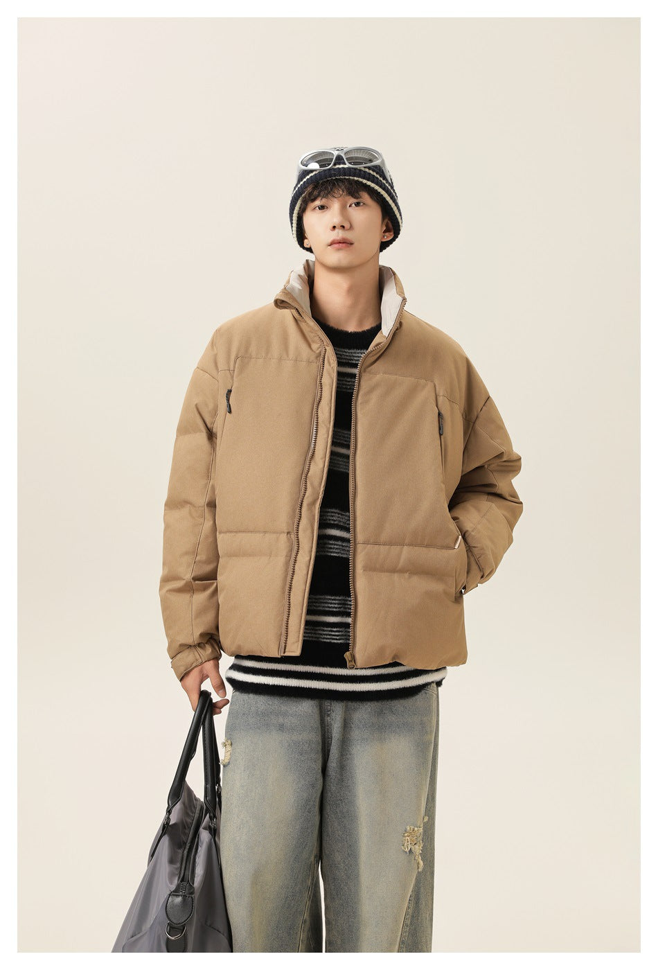 Front view of a model wearing a tan puffer jacket with a high collar, zip front, and multiple pockets.