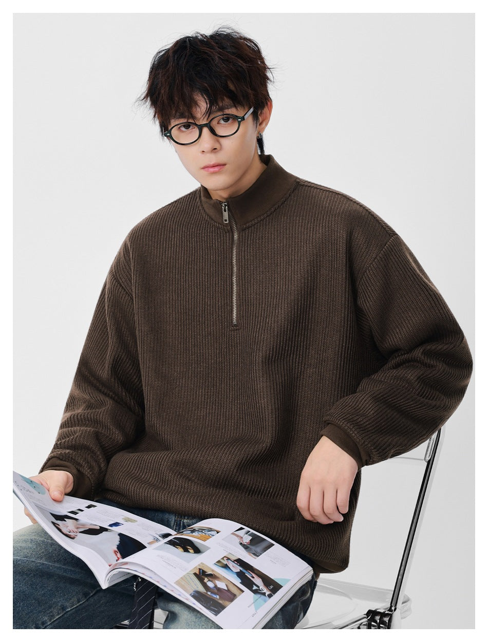 Man seated wearing a brown ribbed half-zip stand-collar pullover while reading a magazine