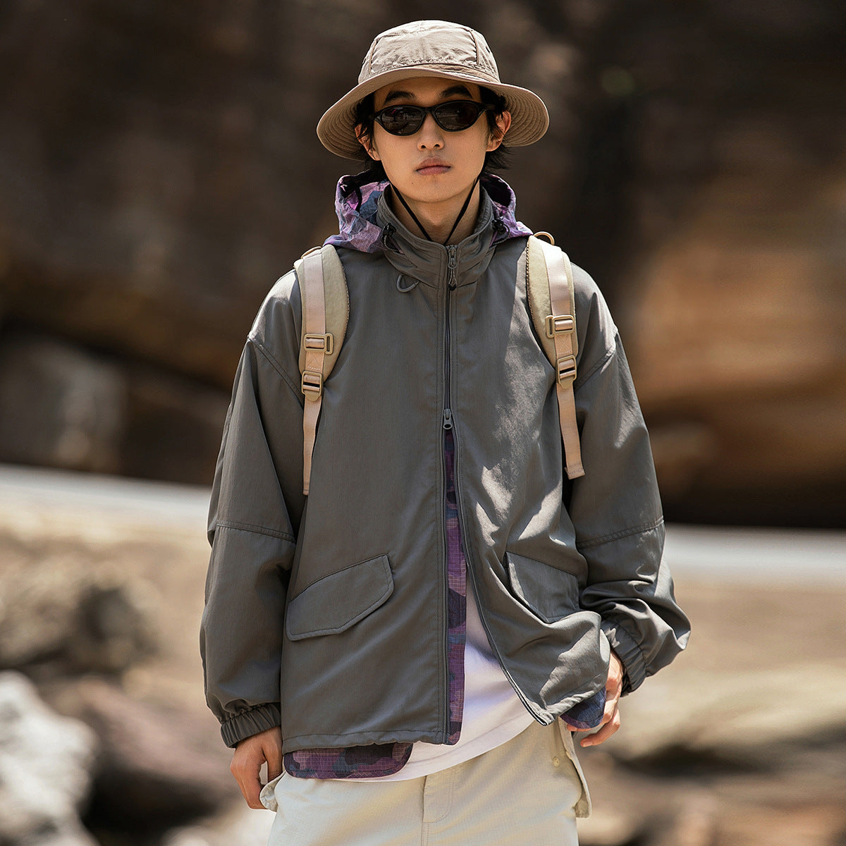 Man wearing a charcoal hooded zip jacket with flap pockets and elastic cuffs.