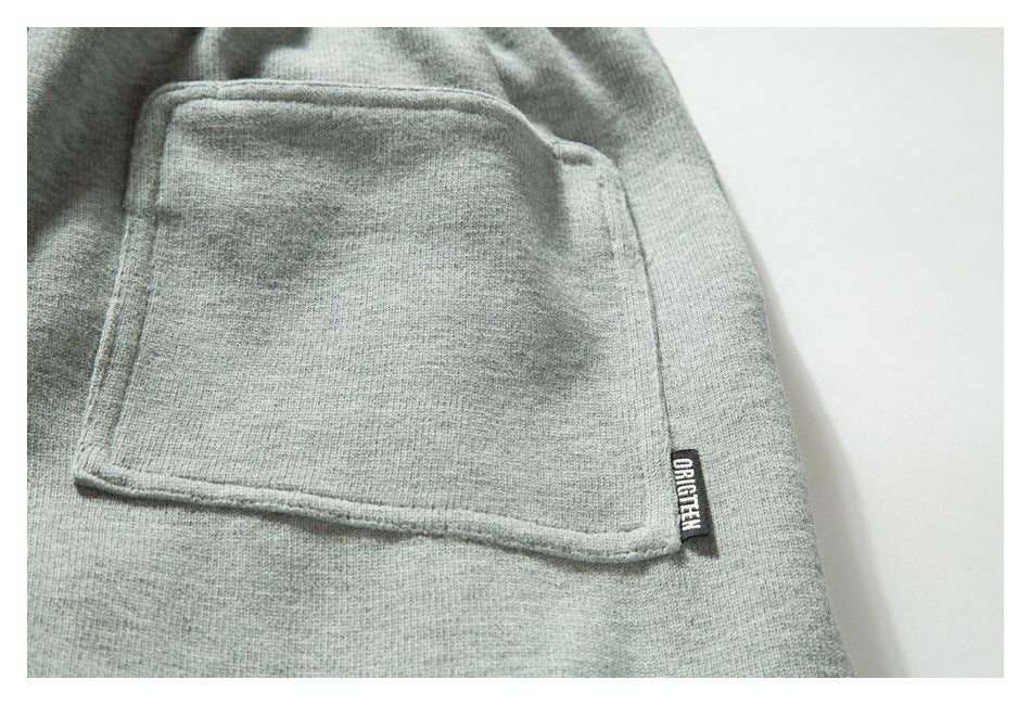 Close-up of a rectangular pocket and small sewn label on light gray knit joggers.