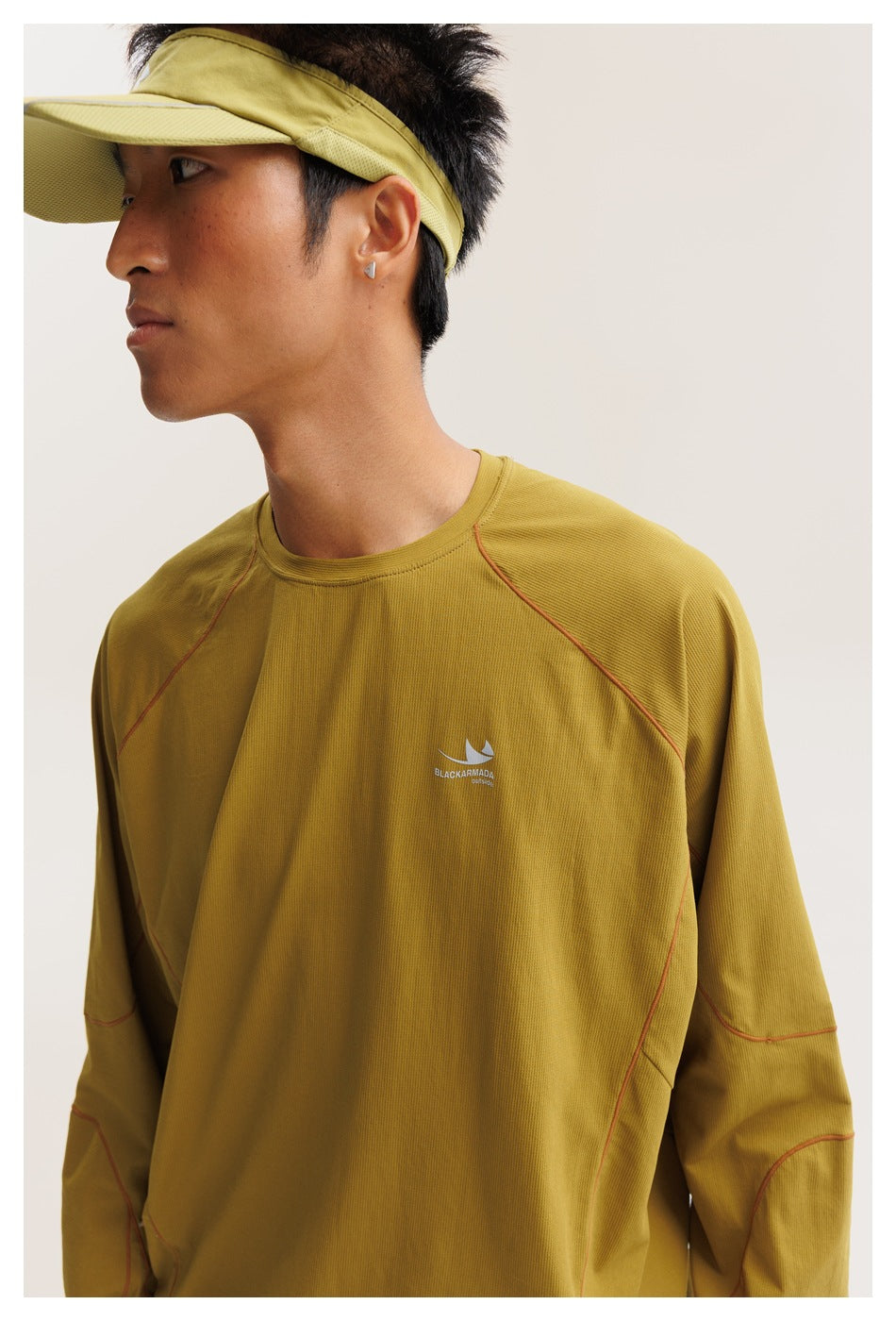 Close view of a model wearing a mustard-yellow long-sleeve top with red seam accents and a small chest emblem.