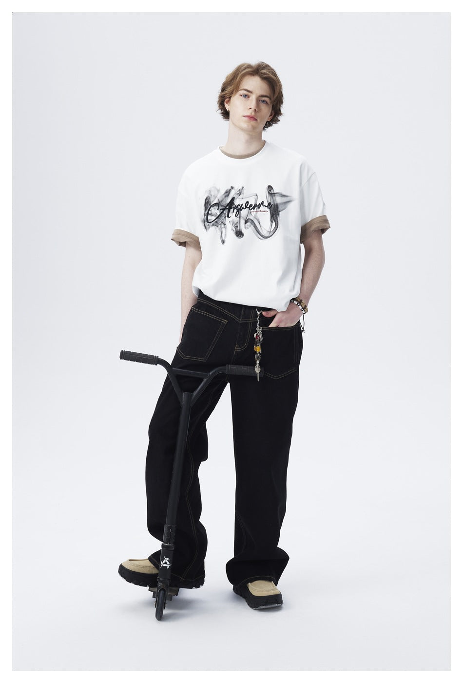 Model wearing a white graphic T-shirt with tan sleeve cuffs and black wide-leg jeans.
