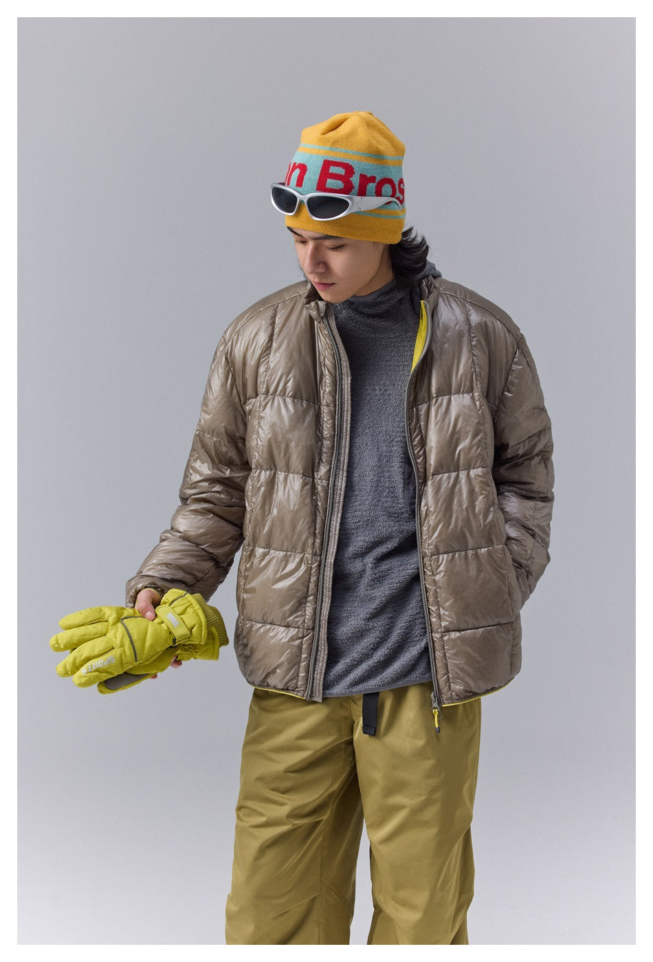 Model wearing a taupe quilted jacket and holding yellow gloves, shown from the front.