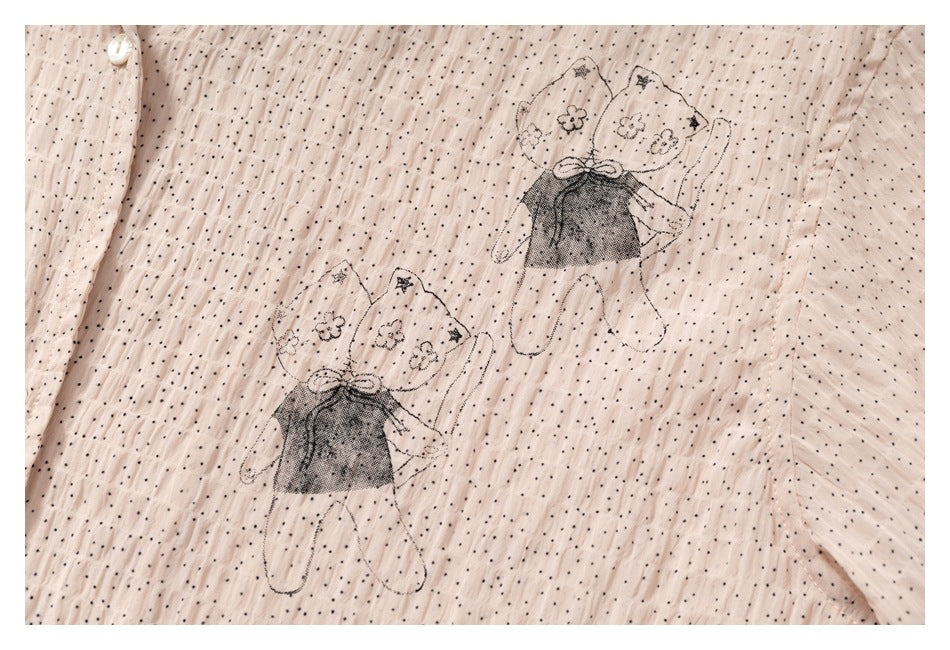 Close-up of pale blush fabric with tiny black dots and two illustrated girls wearing floral headscarves.