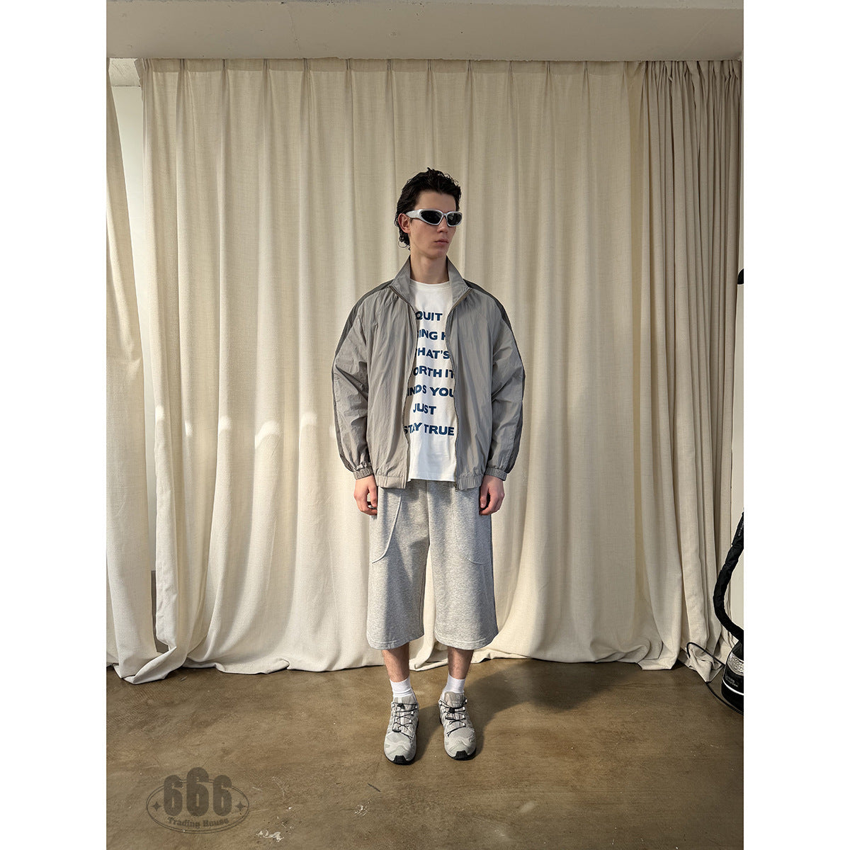 Full-length front view of a model wearing light gray knee-length shorts with curved pockets and a gray jacket.