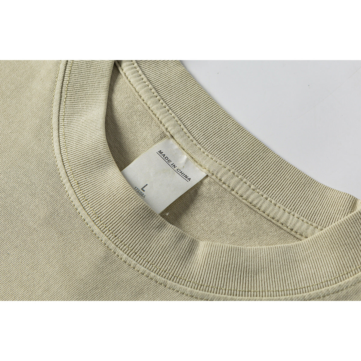 Close-up of a beige T-shirt's ribbed crew neckline, stitching, and inner label marked “Made in China.”