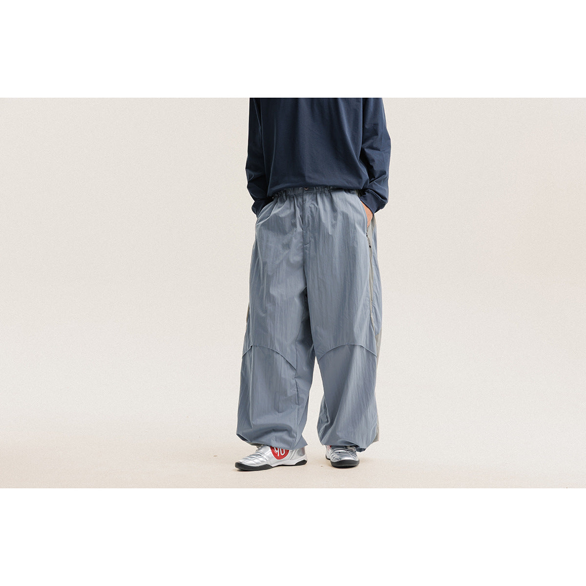 Front view of a model wearing loose light blue-gray pants with curved knee seams and a gathered waist.