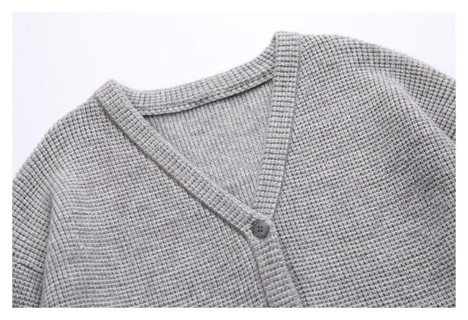 Close-up of a gray cardigan's textured knit, V-neck trim, and button closure.