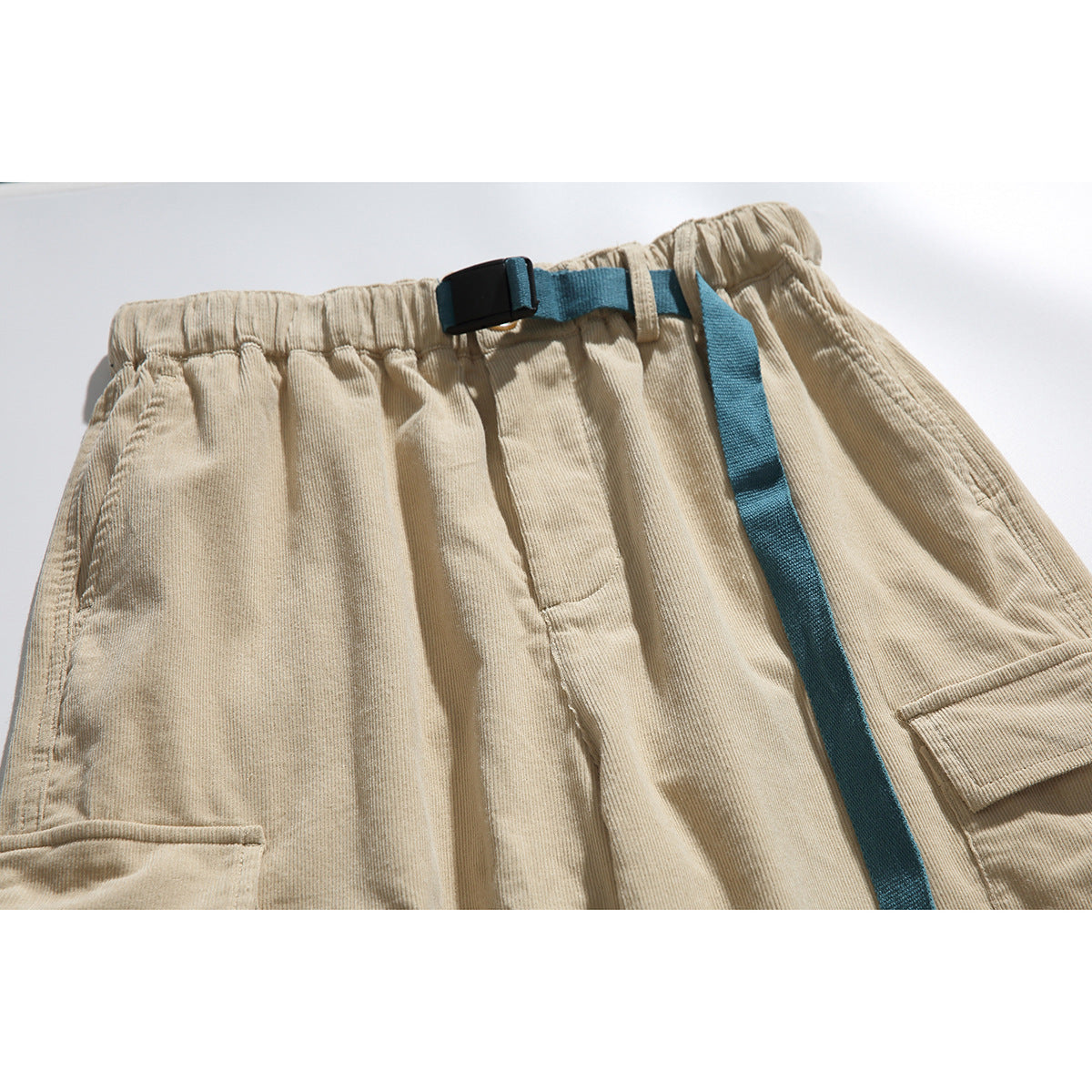 Close-up of beige cargo pants showing the elastic waist, teal belt strap with black buckle, and flap pockets.