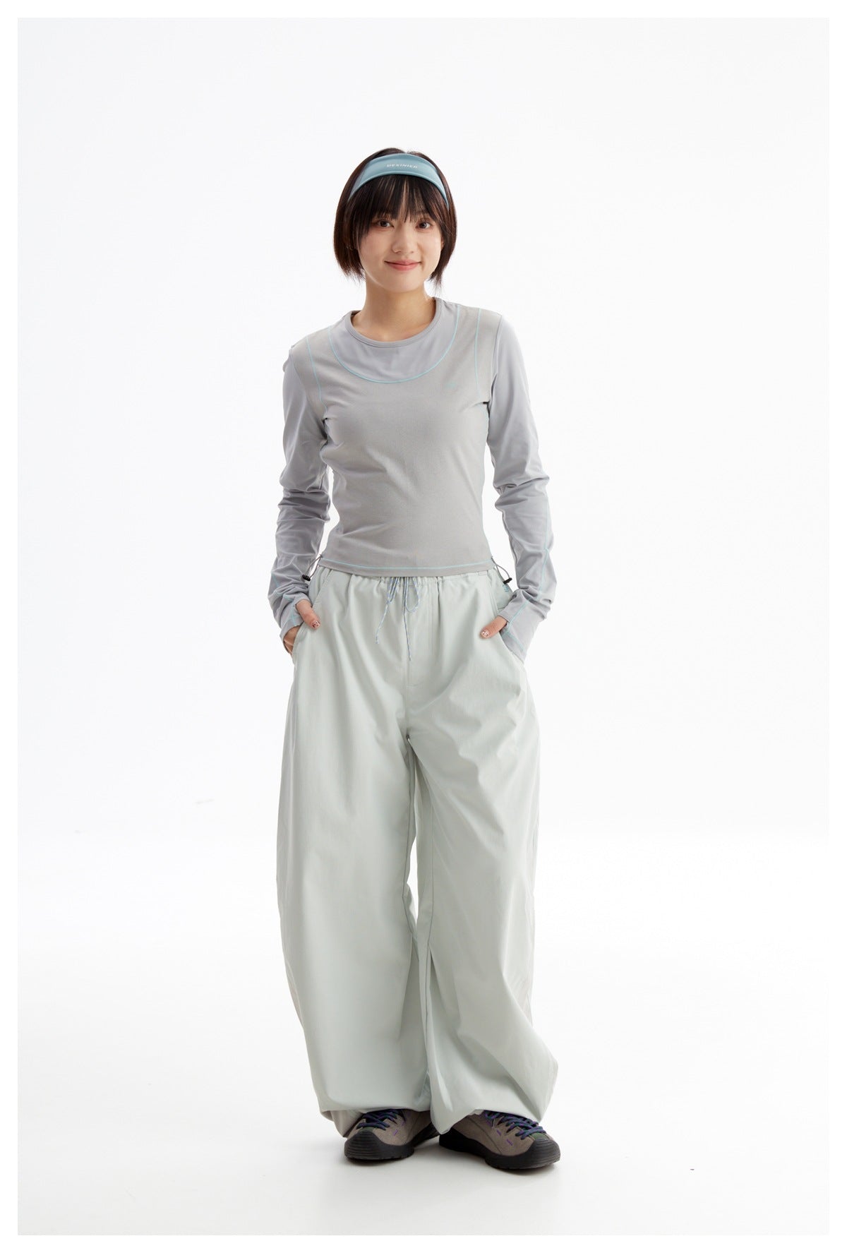 Model wearing a light gray long-sleeve top with teal piping and pale mint wide-leg pants, shown from the front.