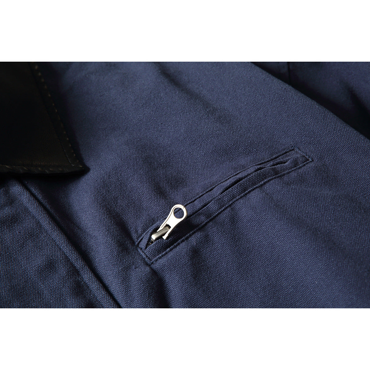 Close-up of a slanted zip pocket with a silver zipper on navy jacket fabric.
