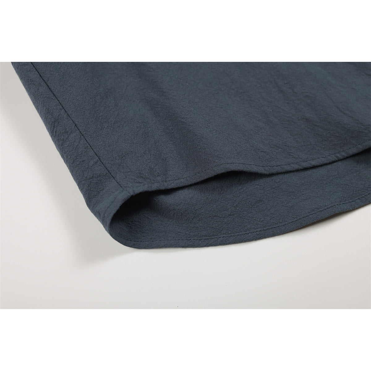 Close-up of the curved, double-stitched hem on a dark slate shirt.