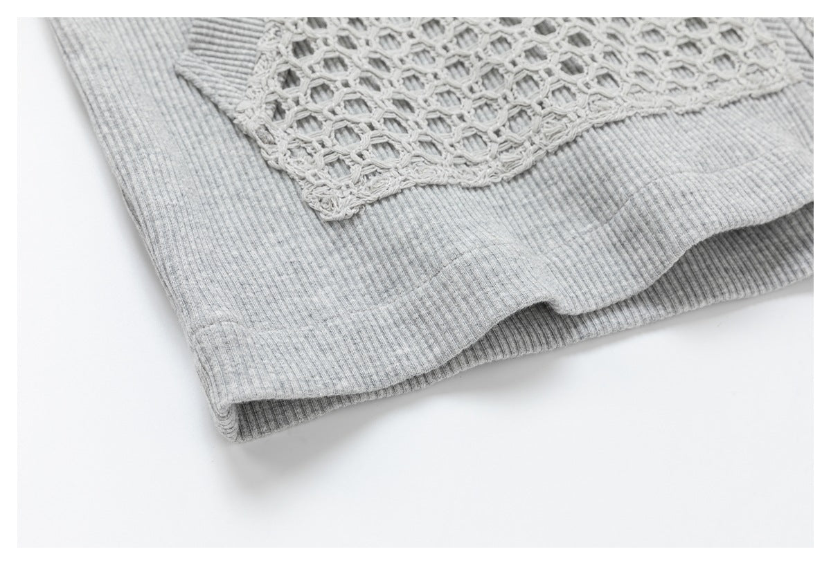 Close-up of the ribbed hem and edge of an openwork crochet panel on a light gray garment.