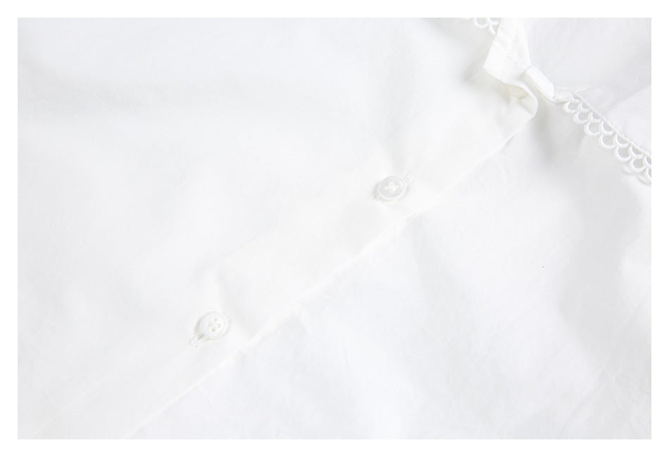 Partial close-up of a white shirt front with two white buttons and a scallop-trimmed collar edge.
