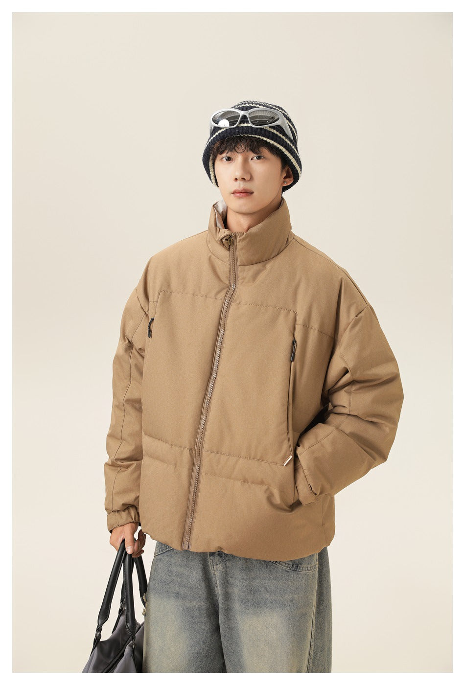 Model wearing a tan padded jacket with a high collar, front zip and zippered pockets.