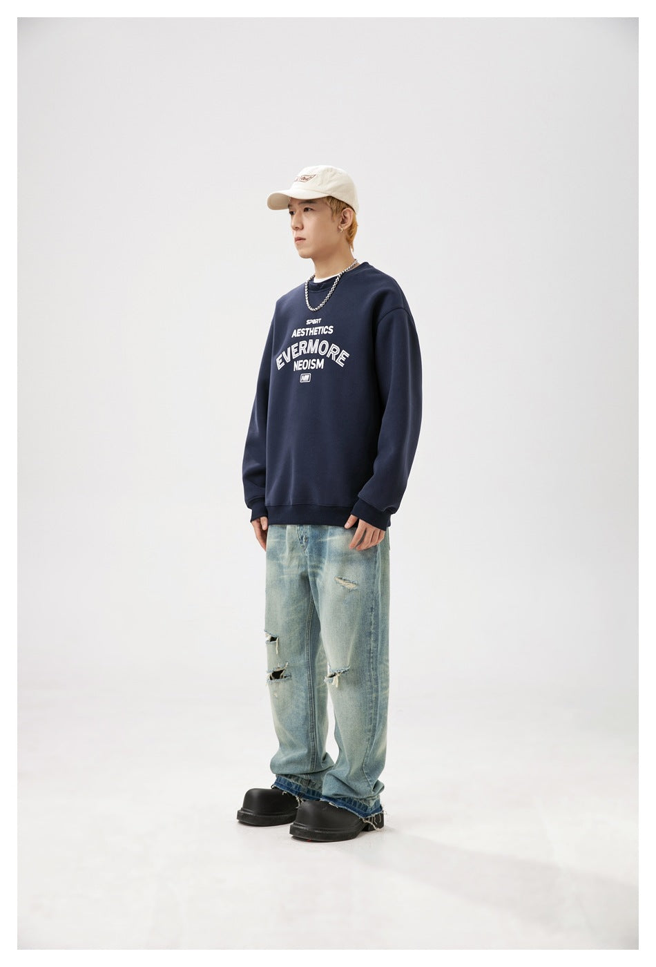 Three-quarter view of a model wearing a navy graphic crewneck sweatshirt and distressed light blue jeans.