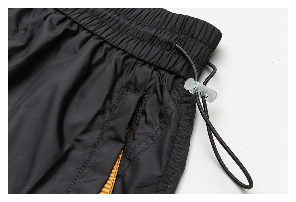 Close-up of black shorts showing the gathered waistband, side drawcord and toggle, and zip pocket with orange trim.