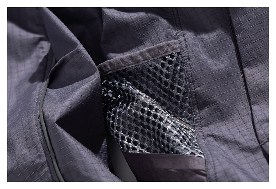 Close-up of a charcoal jacket's open mesh pocket against grid-patterned fabric.