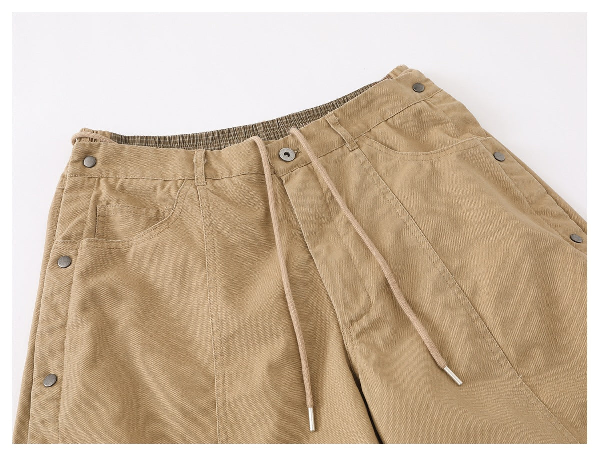 Close-up of tan pants showing a drawstring waist, front pockets, and metal snap details.