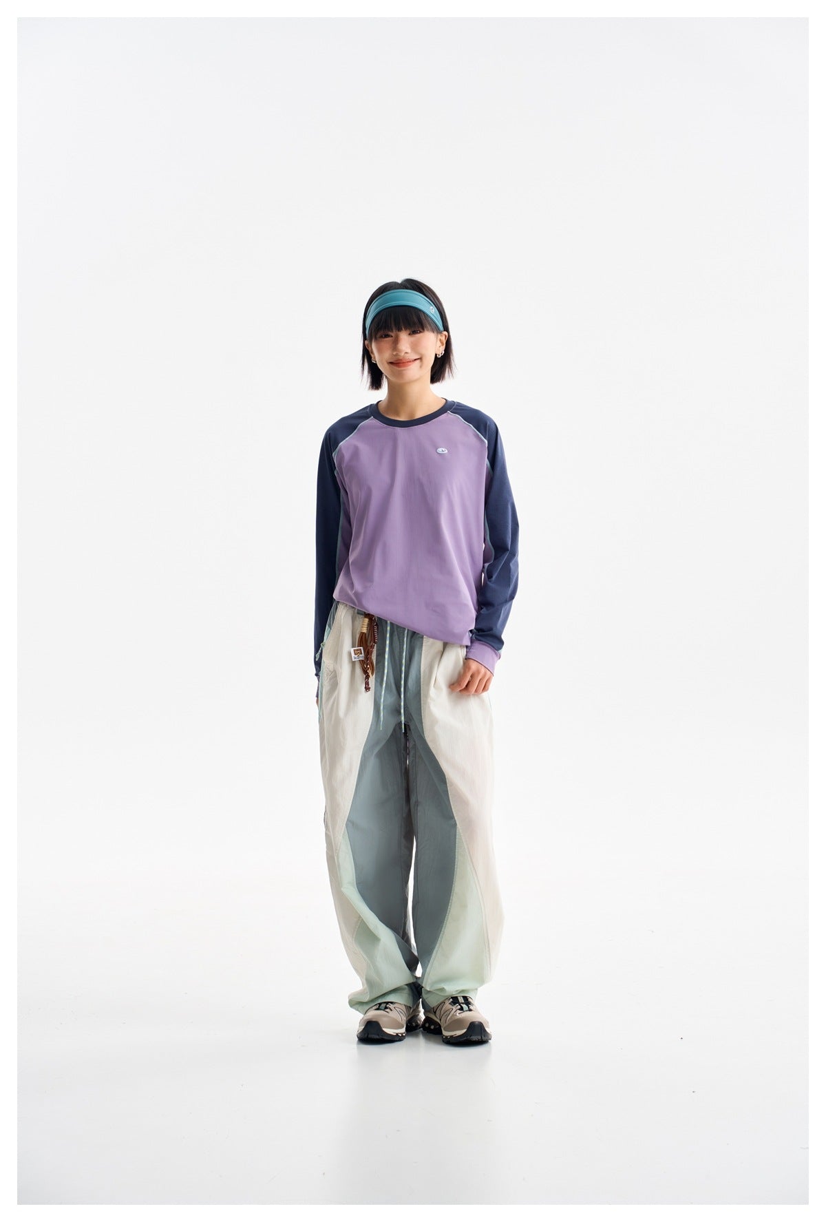 Model in a lavender top with navy sleeves and loose color-blocked pale pants, facing forward.