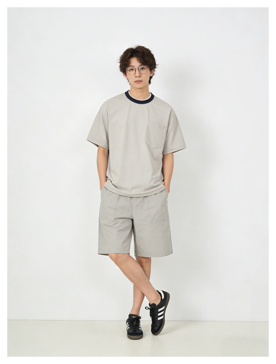 Model wearing a light gray short-sleeve T-shirt with a chest pocket and dark contrast collar, with matching shorts.