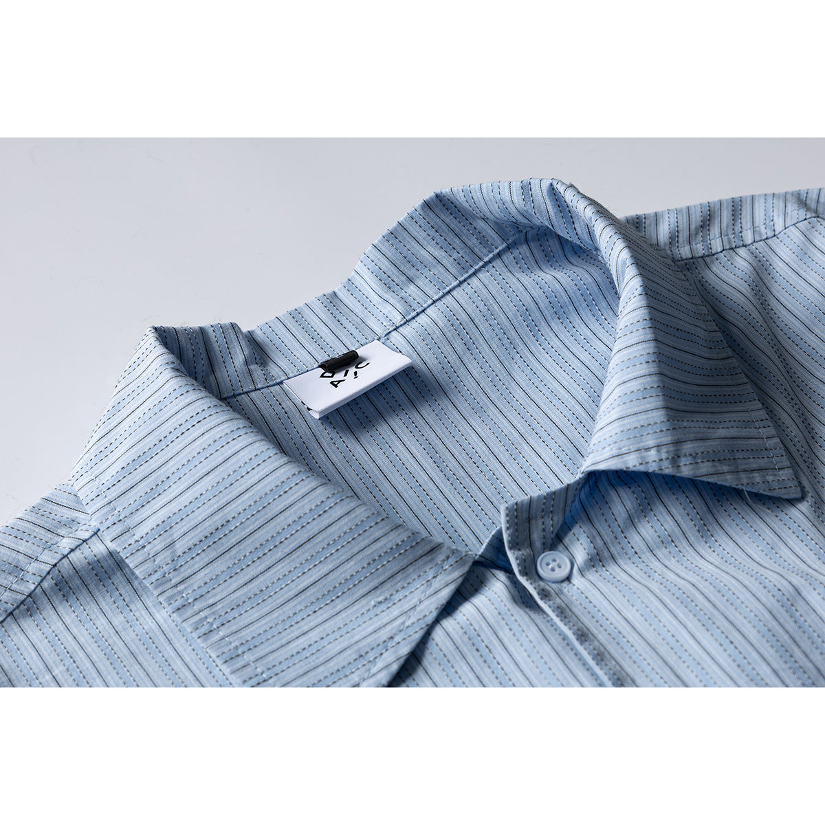 Close-up of a pale blue striped short-sleeve shirt collar, placket button, and attached neck tag.