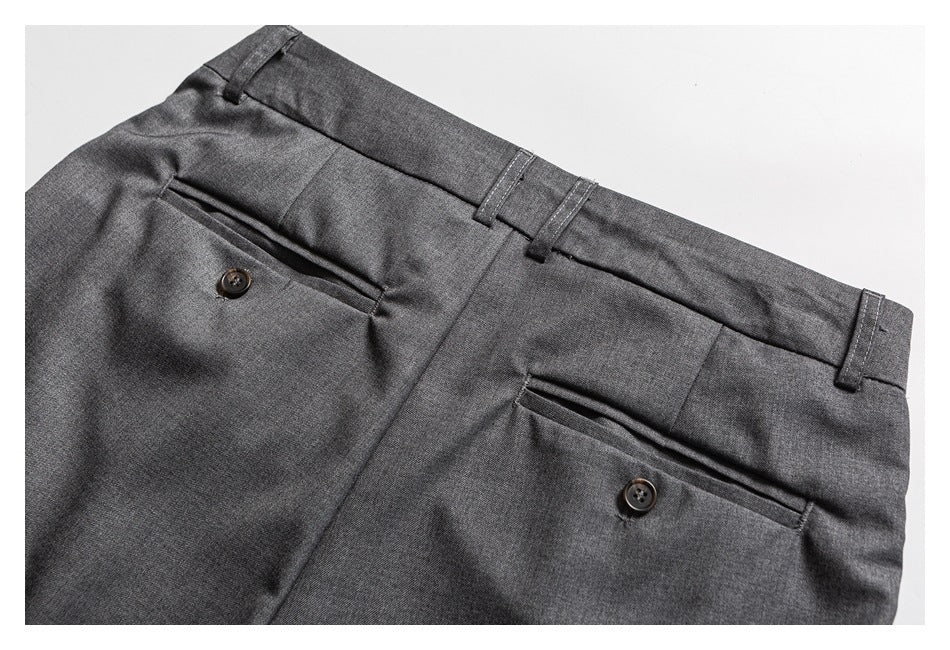 Close-up of gray trousers showing the waistband, belt loops, and two buttoned welt pockets.