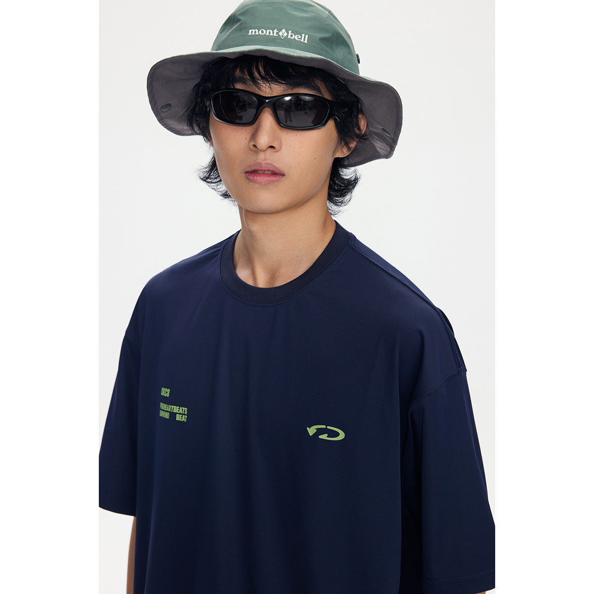 Close-up of a model wearing a navy T-shirt with small lime chest graphics and a green bucket hat.