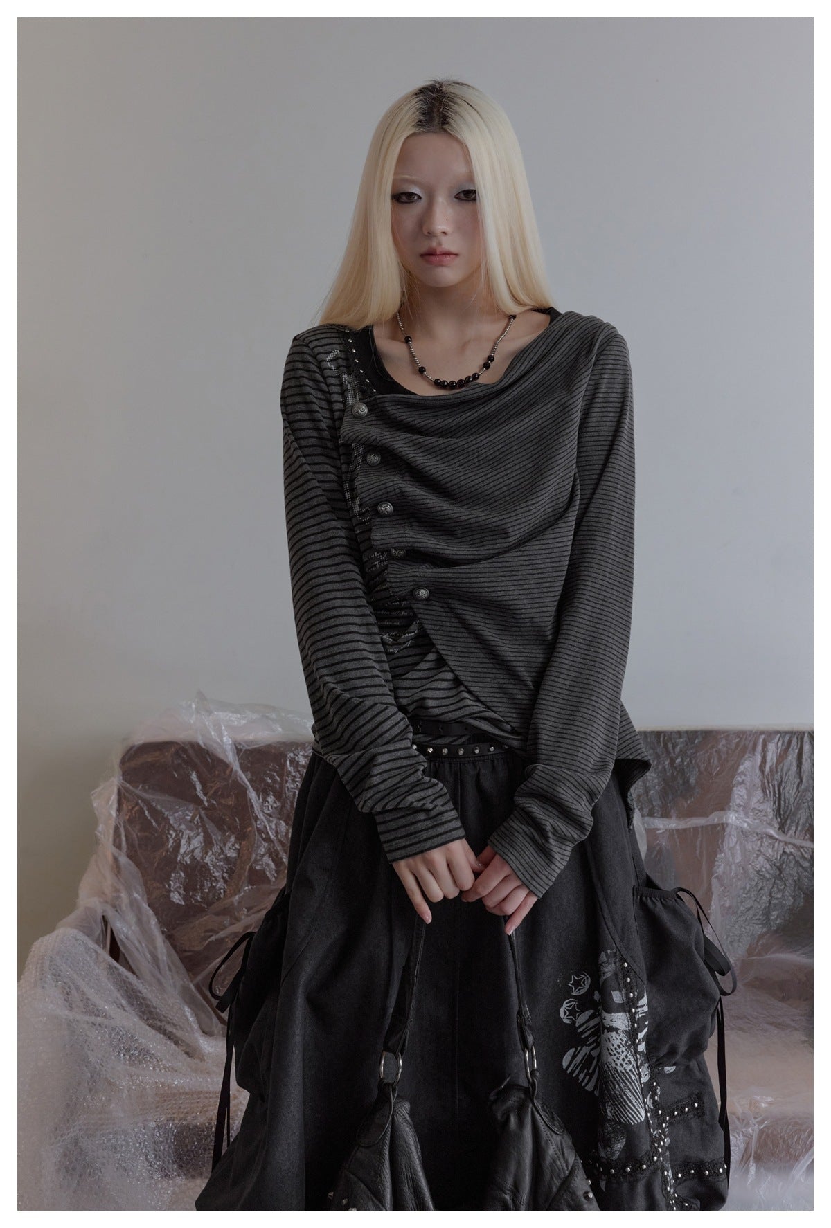 Front view of a model in a charcoal striped top with an asymmetric draped front and button detailing.