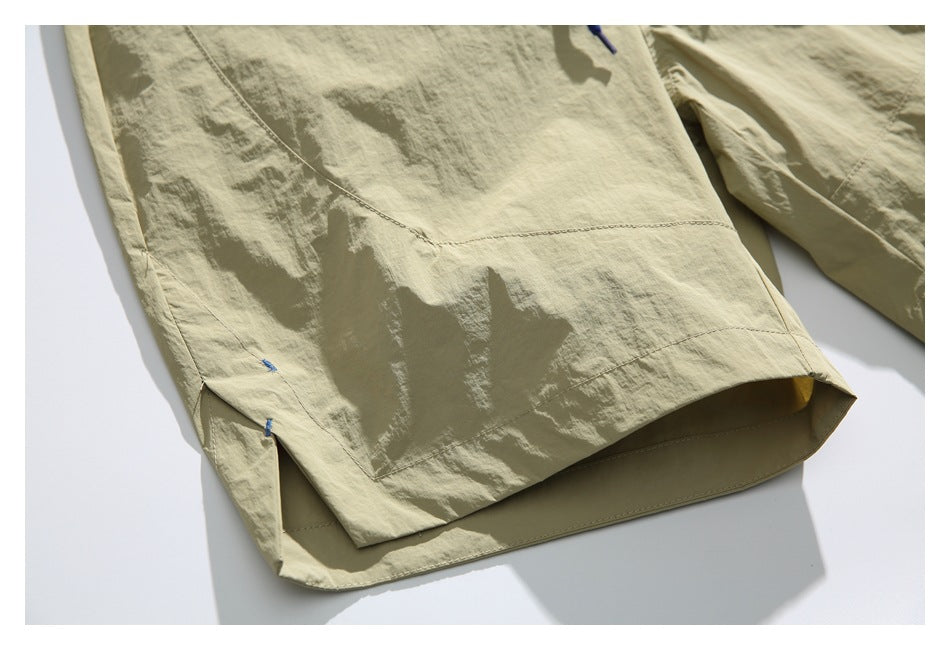 Close-up of a light khaki garment hem with a side slit, visible stitching, and small blue bartacks.