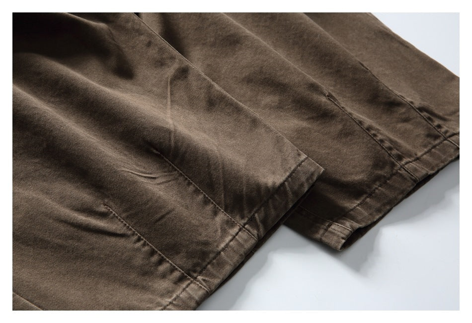 Close-up of brown trousers showing overlapping hems, stitching, and seam details.