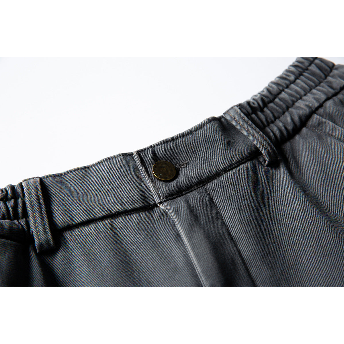 Close-up of charcoal-gray pants showing the elasticated waistband, belt loop, and dark front button.