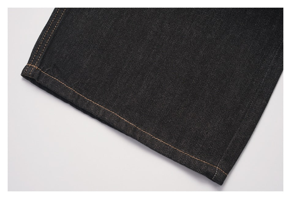 Close-up of a dark denim jeans leg hem with tan contrast stitching.