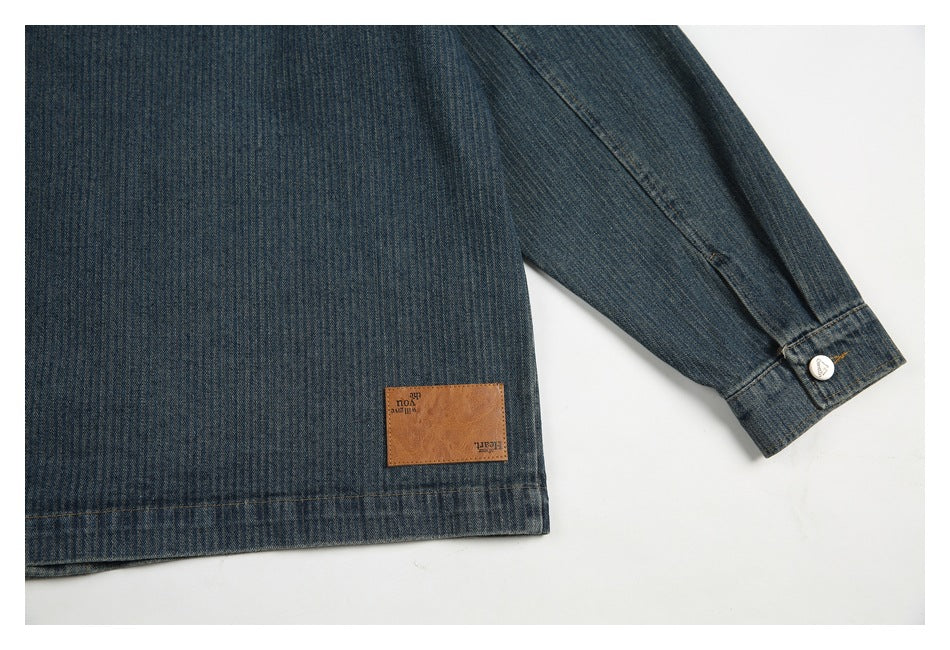 Back view of a dark blue denim jacket laid flat, showing a leather hem patch and buttoned cuff.