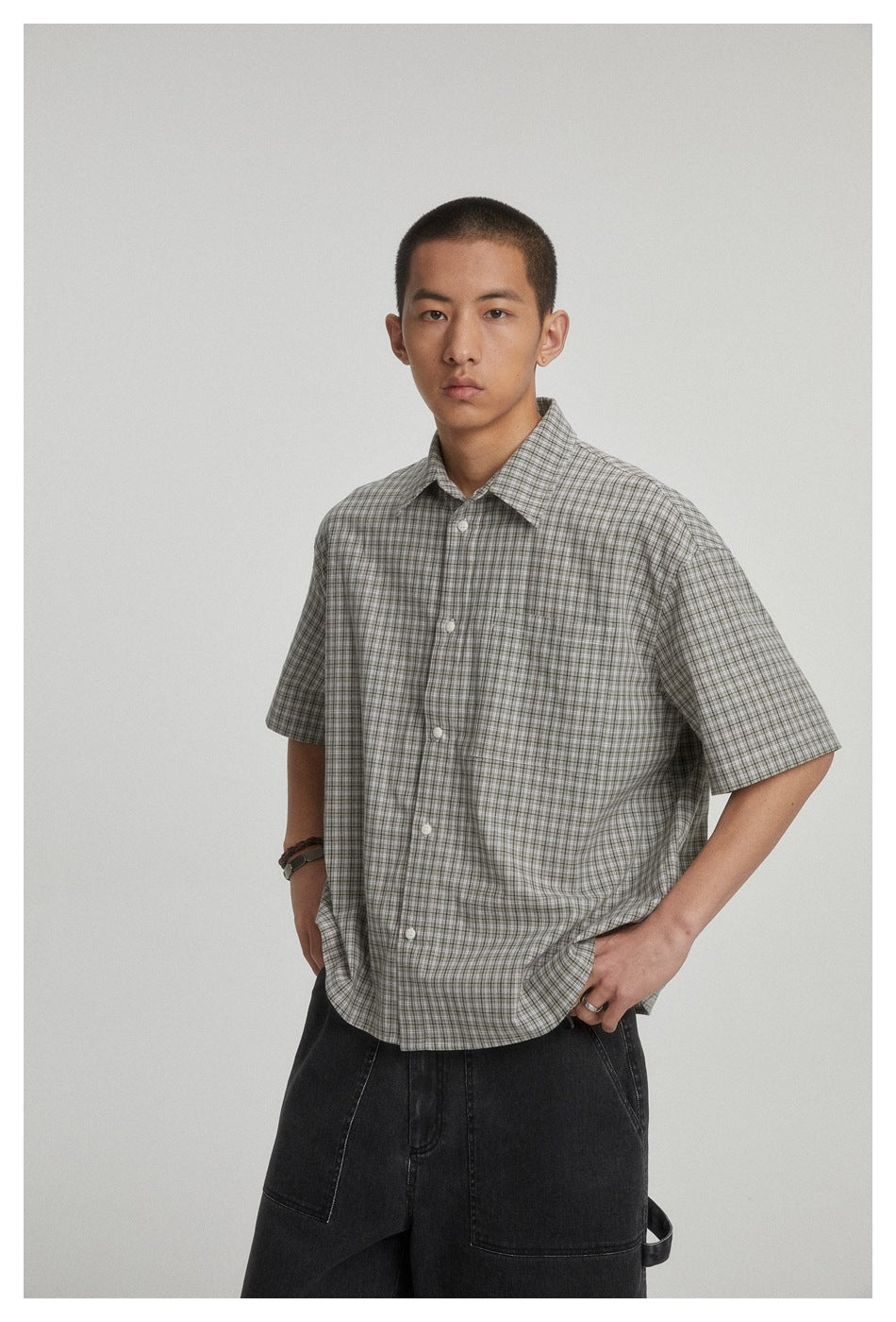 Closer view of a model wearing a gray plaid short-sleeve button-up shirt with a pointed collar and chest pocket.