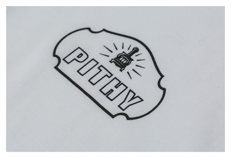 Close-up of an outlined badge graphic with a small illustration and block lettering on white fabric.