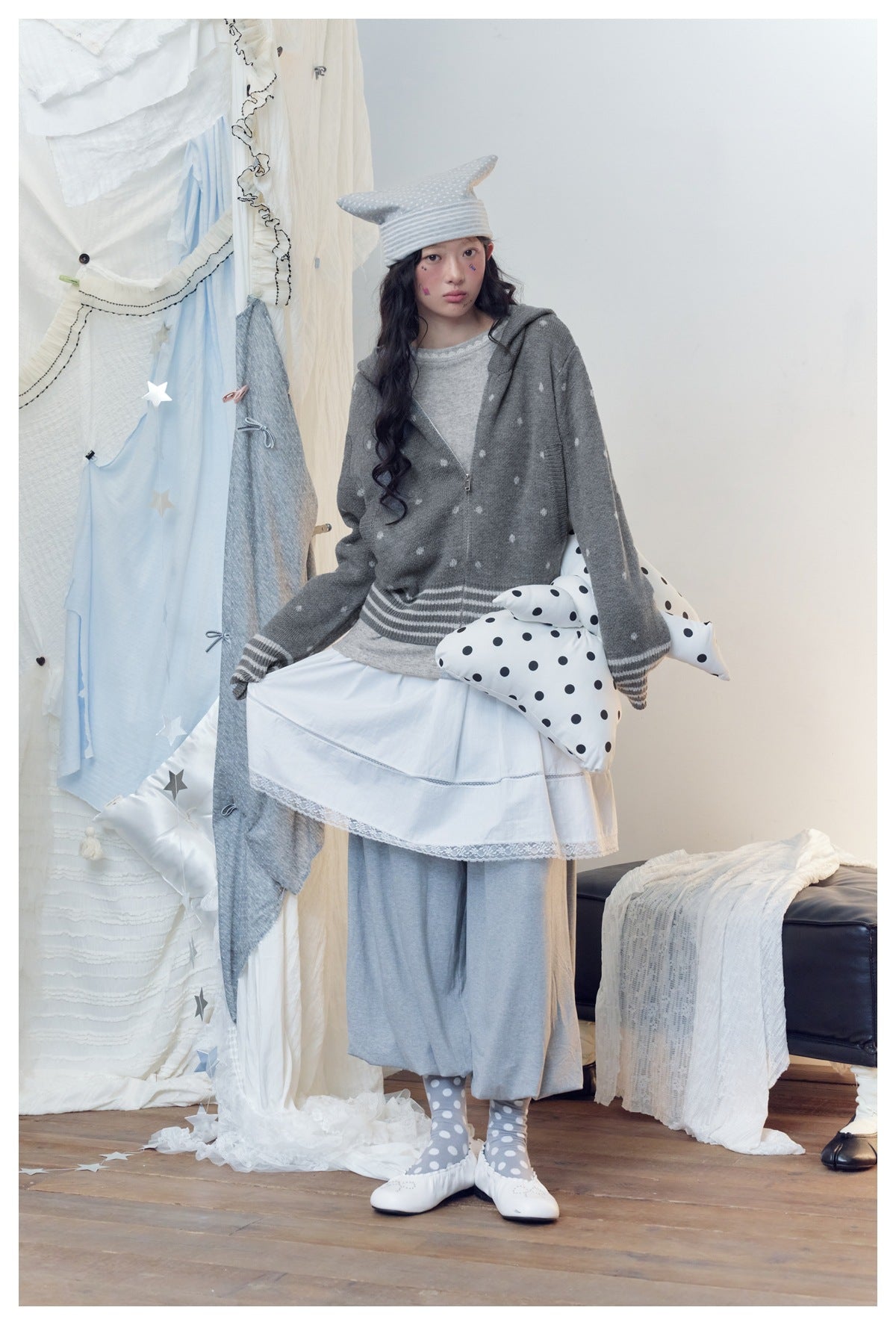 Full-length model wearing a gray spotted zip hoodie over a white lace-trim skirt and loose gray pants.