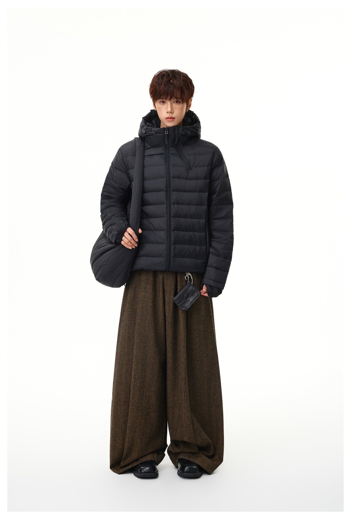 Front view of a model wearing a black hooded quilted jacket with wide brown trousers.