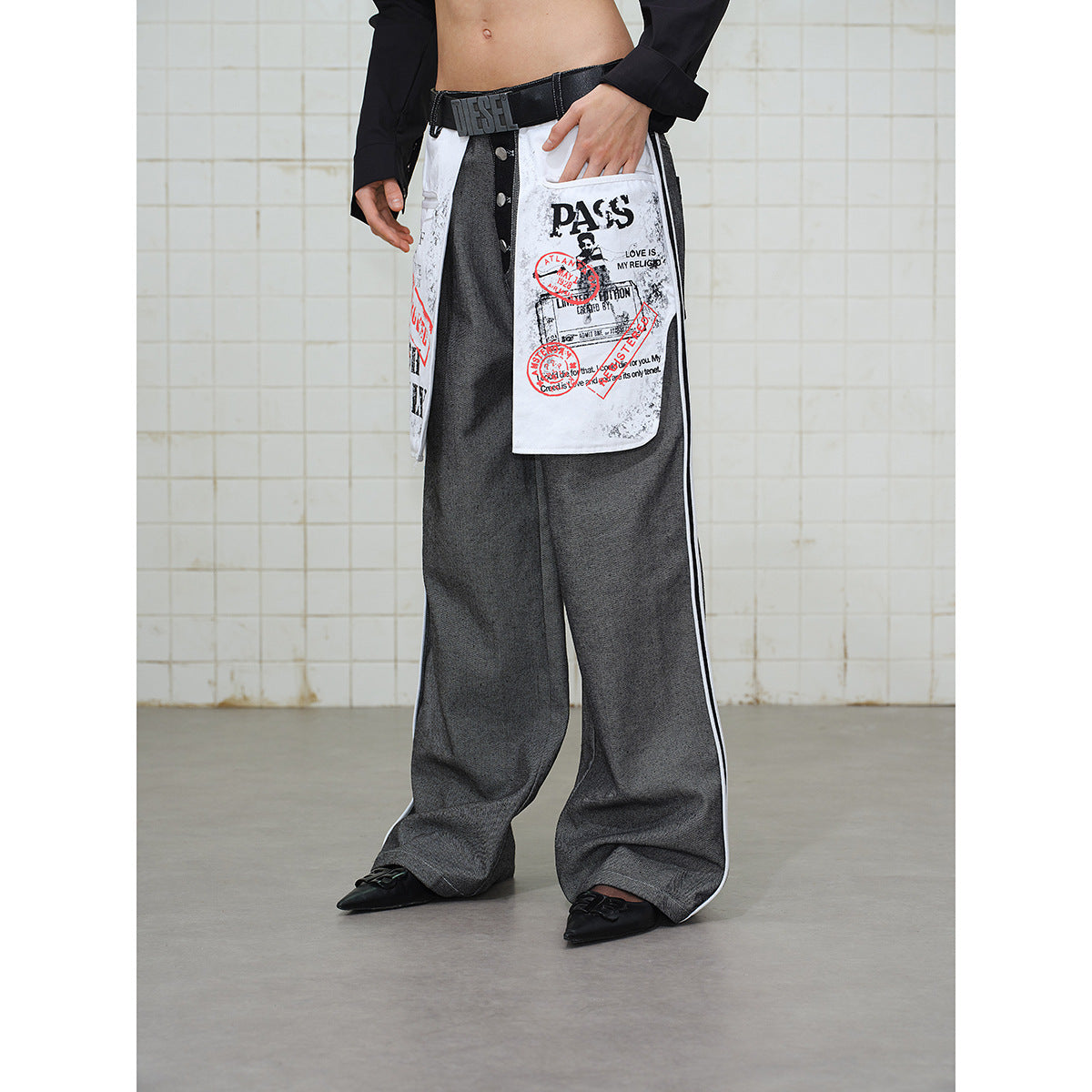 Model wearing wide gray trousers with white graphic front panels, white side stripes, and a black belt.